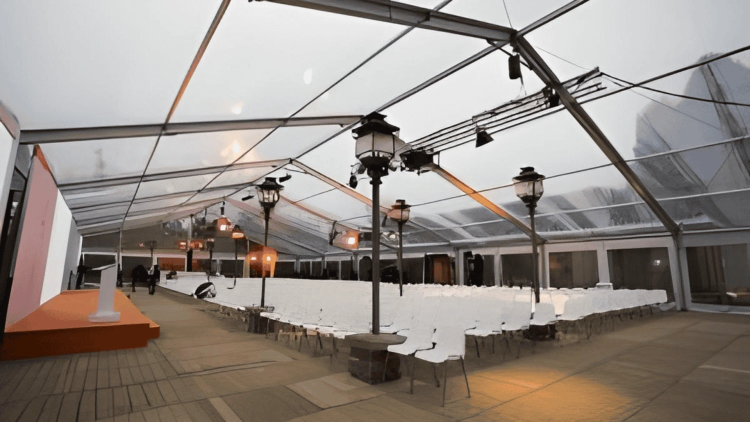 Carpa acristalada con sillas dispuestas para un evento al aire libre con iluminación y decoración elegante.