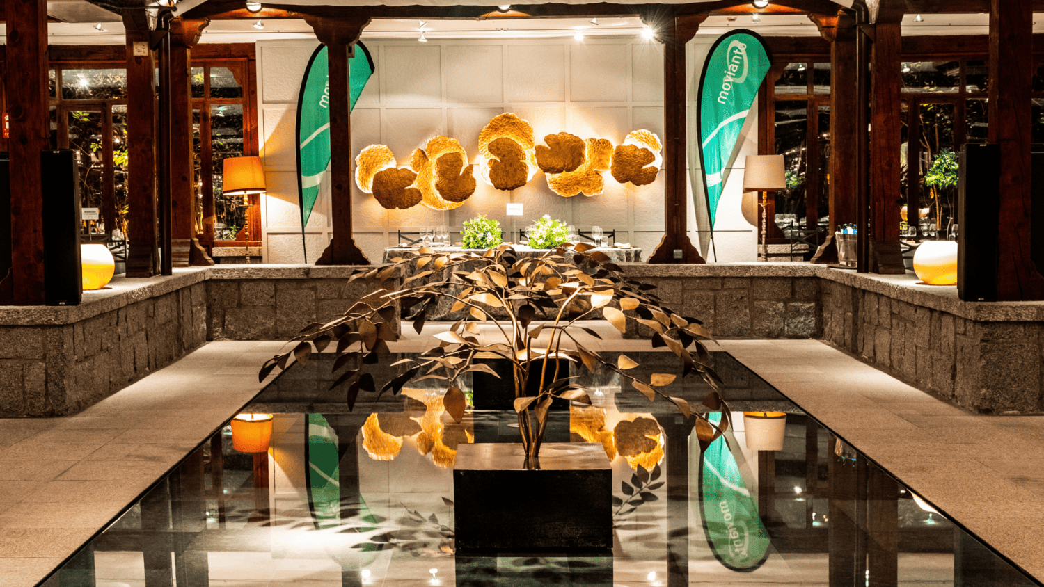 Área de recepción decorada con una planta metálica y banderas de Moriana en un evento elegante.