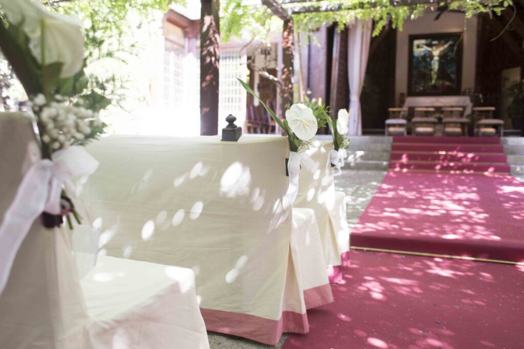 Bancos con fundas blancas y flores blancas junto a una alfombra roja en La Quinta de Illescas