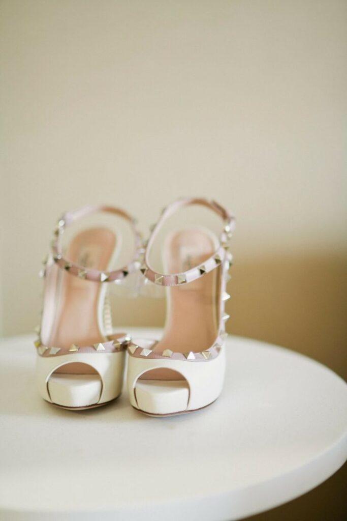 Sandalias blancas de tacón con detalles de tachuelas, colocadas sobre una mesa blanca.