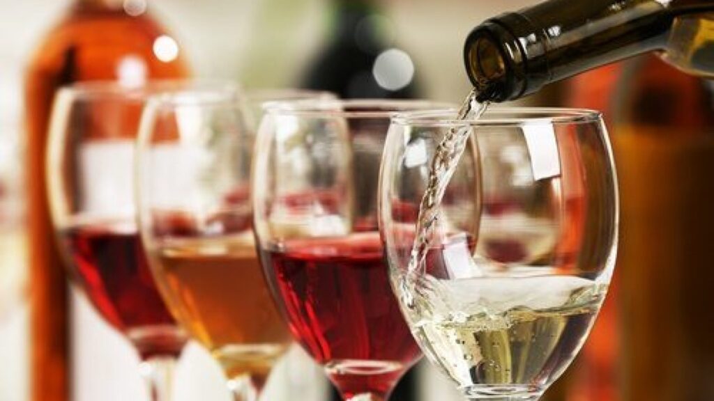 Vino siendo servido en copa junto a otras copas de vino.