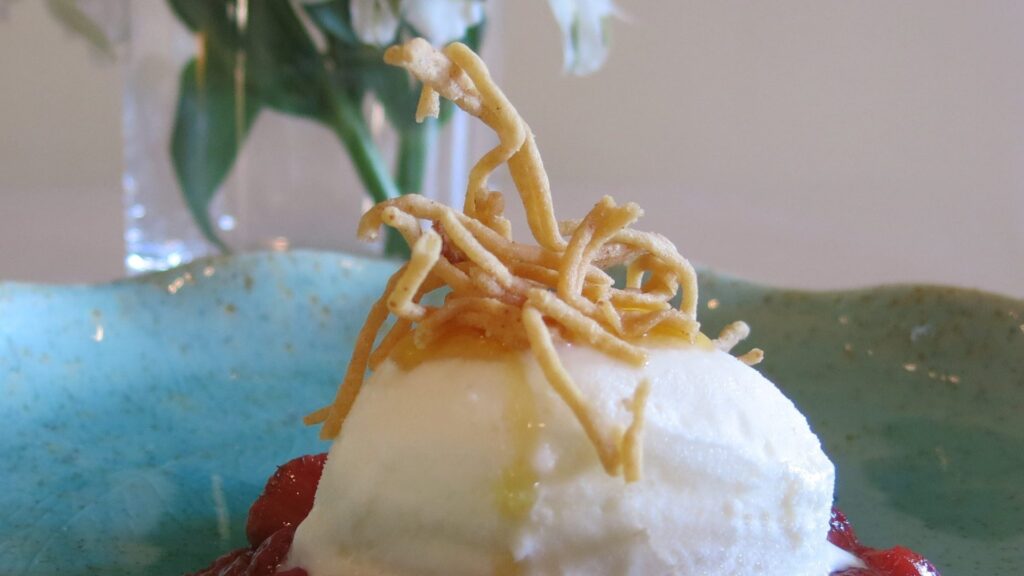 Postre con helado y crujiente sobre plato azul.