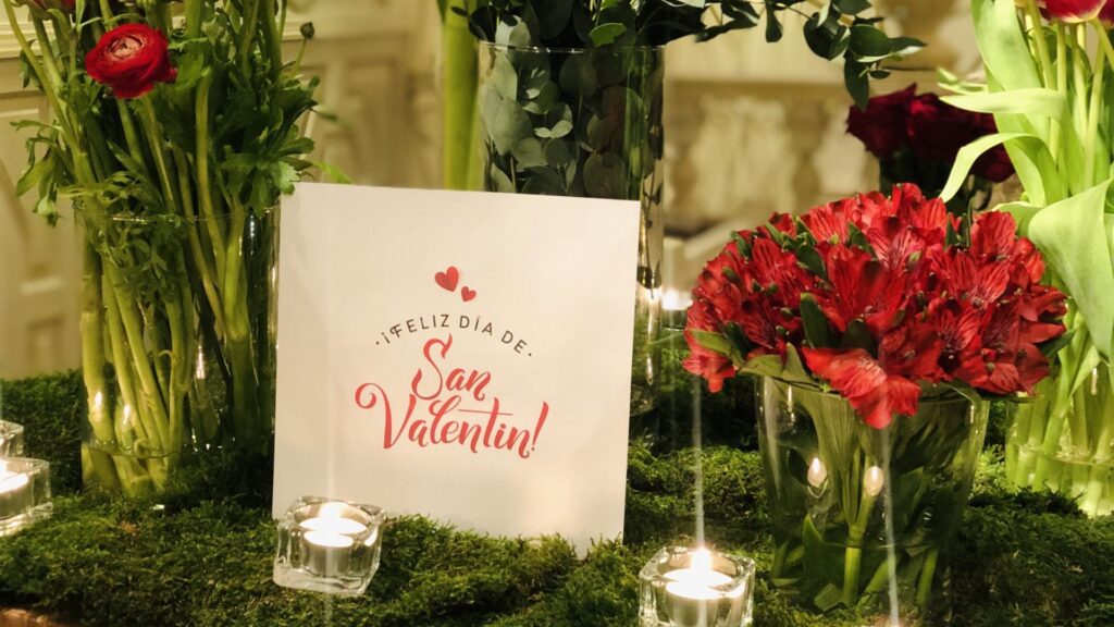 Tarjeta de San Valentín junto a flores rojas y velas.