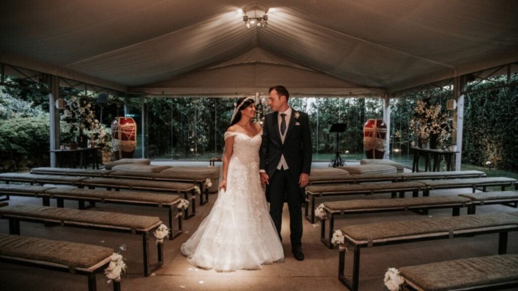 Novios de pie en un altar con bancos y flores.