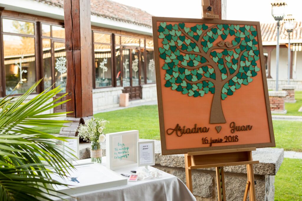Árbol de huellas personalizado para la boda de Ariadna y Juan el 16 de junio de 2018, en La Quinta de Illescas. El cartel con diseño de árbol está decorado con huellas de los invitados, ubicado en un entorno al aire libre junto a una mesa de firmas.