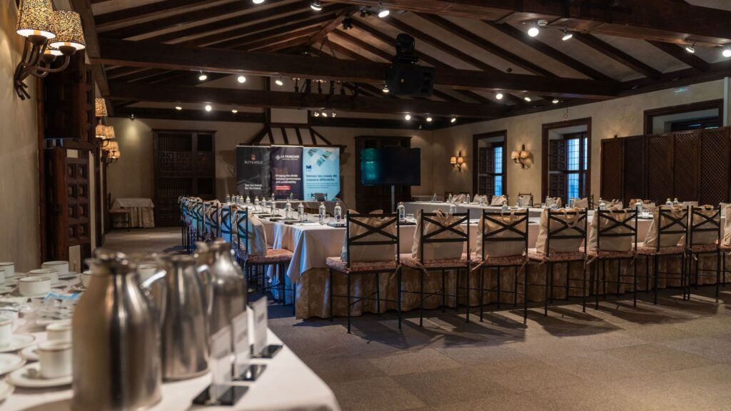 Comedor elegante con mesas redondas preparadas para banquete, lámparas colgantes y sillas en el evento Private Banking Experience de RankiaPro, mayo 2024, La Quinta de Illescas