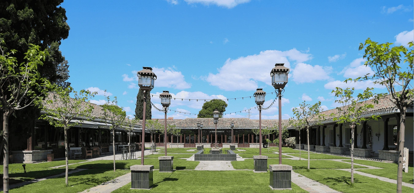 Patio de Los Porches de La Quinta de Illescas con césped, farolas y galerías porticadas a ambos lados