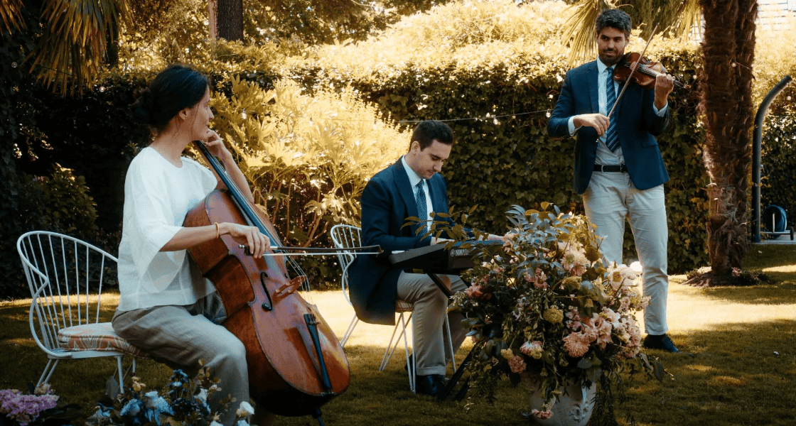 Trío de músicos con violín, chelo y teclado tocando en directo en el jardín de La Quinta de Illescas