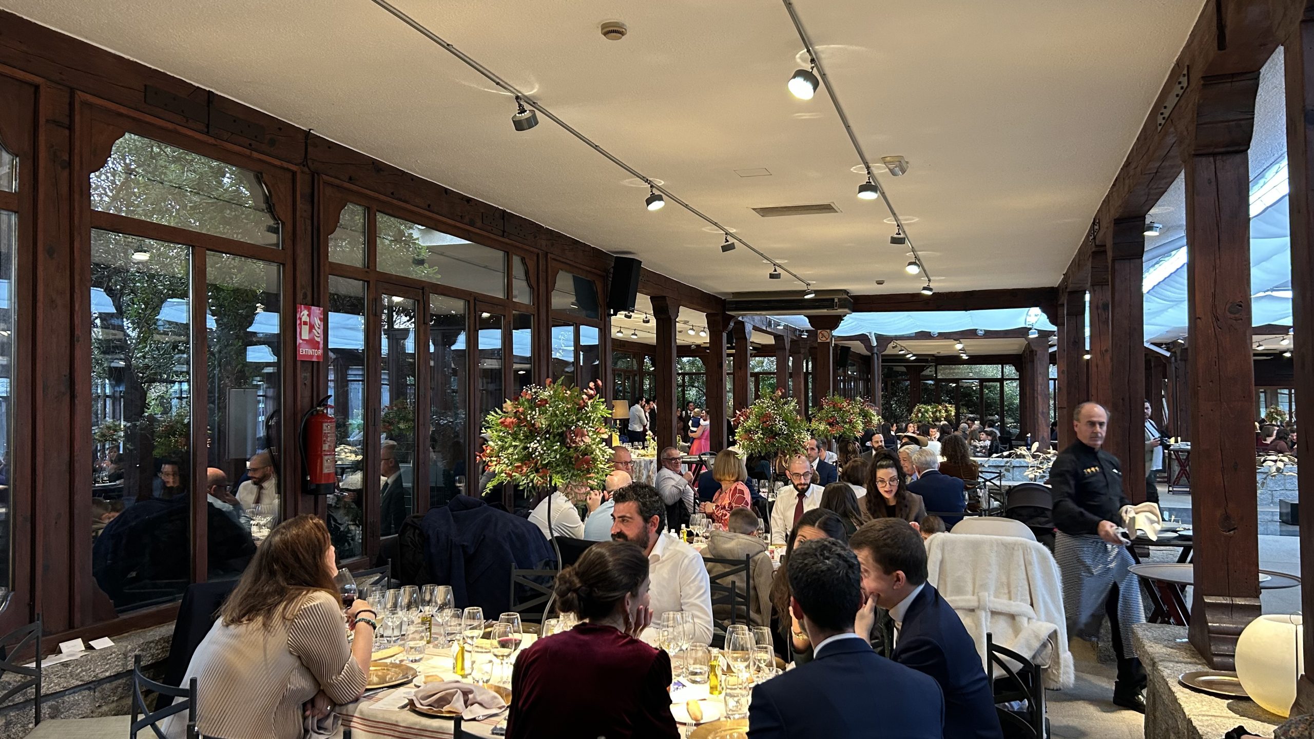 Banquete de boda en el porche acristalado de La Quinta de Illescas con invitados sentados y mesas decoradas con flores